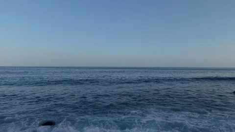 Waves rolling onto a dark boulder shoreline beside a calm open sea in Stock Footage 345183405