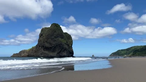 Waves rolling onto an empty summer beach by a large rock. Blue sky and clouds Stock Footage 247896627