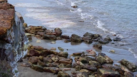 Waves Rolling Into a Multi-Colored Rock Cliff Beach Stock Footage 253534408