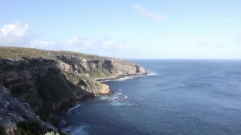 Waves rolling in over coastal cliffs on a sunny day Stock Footage 329665439