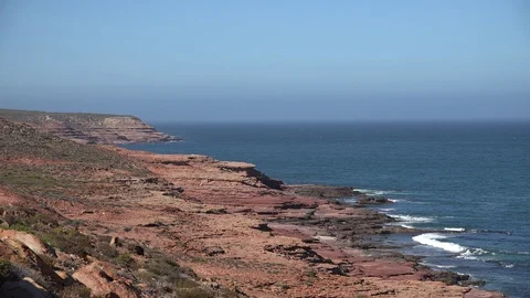 Waves rolling in over red cliffs on a sunny day with the blue ocean Stock Footage 86297393