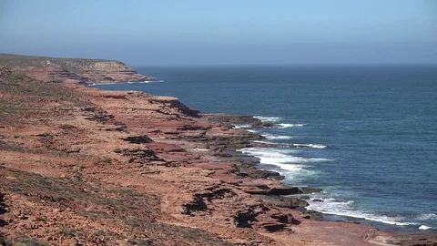 Waves rolling in over red cliffs on a sunny day with the blue ocean Stock Footage 86484858