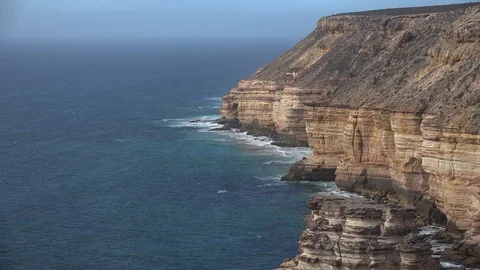 Waves rolling in over steep dramatic red cliff with the ocean in the horizon Stock Footage 86888218