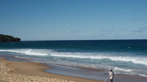 Waves rolling onto a quiet sandy beach with coastal headland and blue sky Stock Footage 317795434