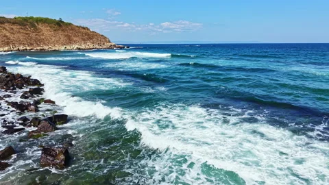 Waves rolling onto the rocky shore under a clear blue sky during daylight at a Stock Footage 344823676