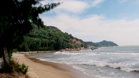 Waves rolling onto sandy beach below green forested headland 库存影片 348545380
