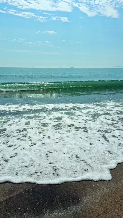 Waves rolling onto the sandy beach with distant ships on the horizon under a Stock Footage 340878214