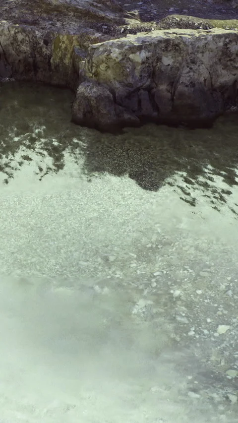 Waves rolling onto a sandy beach near rocks during a cloudy day Video stock 342442993