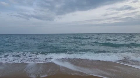 Waves rolling onto sandy beach under cloudy sky with dynamic motion Stock Footage 321651113