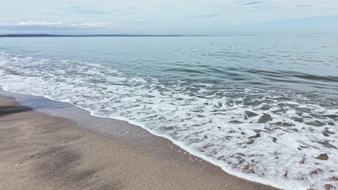 Waves rolling onto a sandy beach while clouds are scattered in the sky during a Stock Footage 335380709
