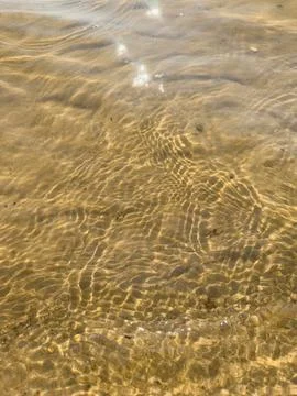 Waves rolling onto sandy shore with sunlight glistening on water surface, t.. Stock Photos