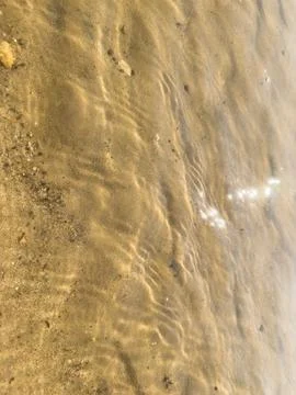Waves rolling onto sandy shore with sunlight glistening on water surface, t.. Stock Photos