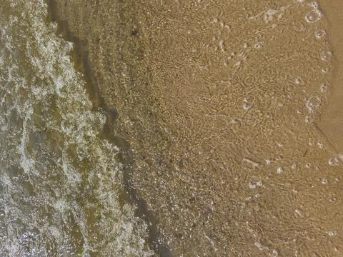 Waves rolling onto sandy shore with sunlight glistening on water surface, t.. Stock Photos