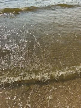 Waves rolling onto sandy shore with sunlight glistening on water surface, t.. Stock Photos