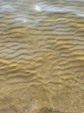 Waves rolling onto sandy shore with sunlight glistening on water surface, t.. Stock Photos