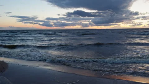 Waves rolling onto sandy shoreline under dramatic sunset sky with dark clouds Stock Footage 345456600