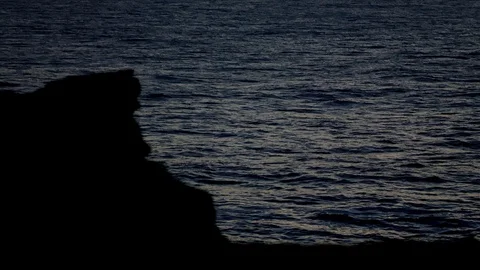 Waves rolling in slow motion with silhouetted cliff in foreground Stock Footage 100798031