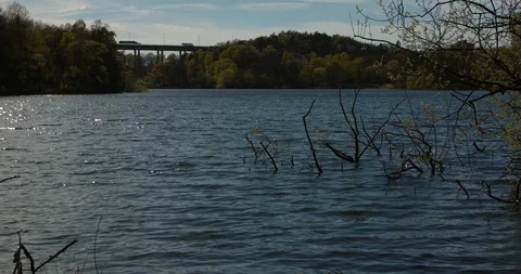Waves rolling in on a small urban lake. Slow motion shot with cars driving on a Stock Footage 94500039