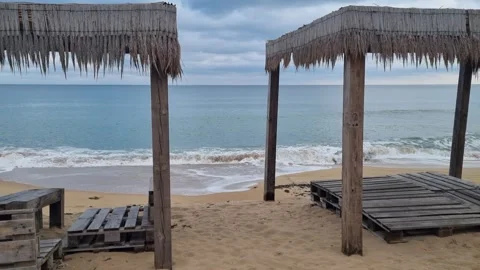 Waves rolling toward beach huts under cloudy sky on empty shore Stock Footage 322124799
