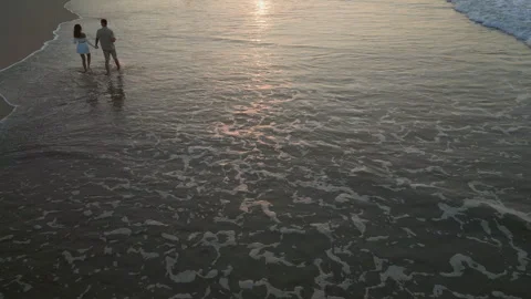 Waves run on sand at sunrise, young couple walks in tide holding hands aerial Stock Footage 248050698