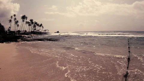 Waves, running into the sand, in the distance high palm trees on the rocks Stock Footage 86698579