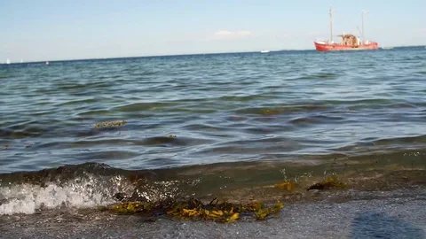 Waves on sand beach in slow motion with red ship in the background Stock Footage 81599197