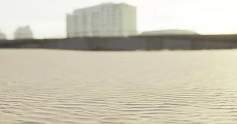 Waves of sand ripple under sunlight on a beach near buildings at dusk Stock Illustration