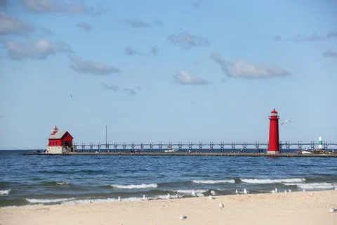 Waves on a sandy beach full of Gulls with the Grand Haven Lighthouse Stock Photos