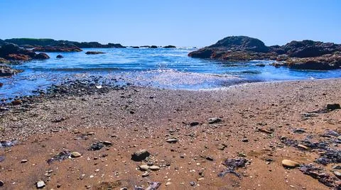 Waves on sandy beach with shiny pieces of glass 스톡 사진