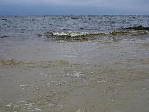 Waves on a sandy shore under a cloudy sky Stock Photos