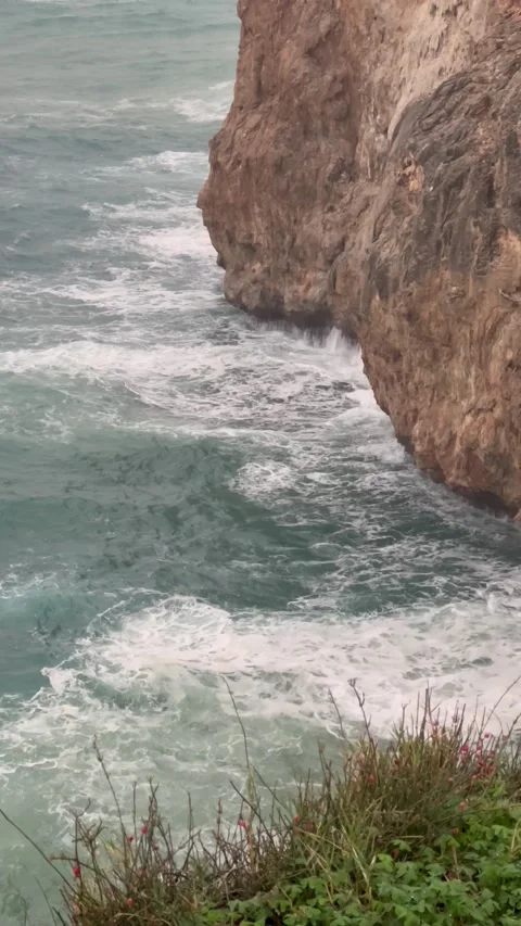 Waves of a sea hitting the rocks by the coast on a rainy day Stock Footage 334404261