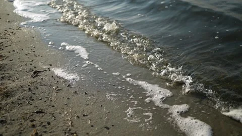 The waves slowly beat against the sandy shore forming foam. Video stock 271583487