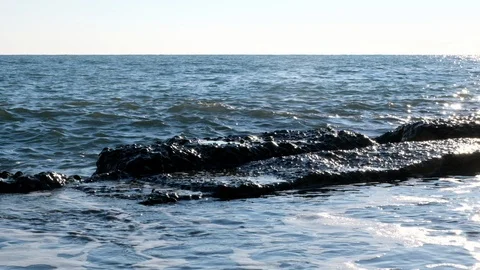 The waves slowly break on the rocks on the shore. Blue sky and water. Vidéo 106373003