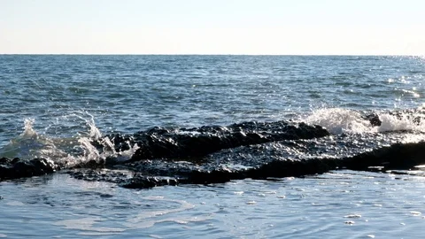 The waves slowly break on the rocks on the shore. Blue sky and water. Vidéo 106374088