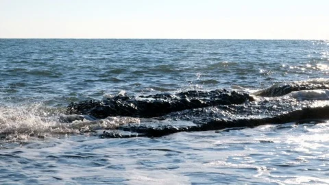 The waves slowly break on the rocks on the shore. Blue sky and water. Vidéo 106374231