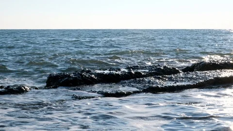 The waves slowly break on the rocks on the shore. Blue sky and water. Vidéo 106374604