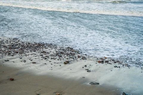 Waves softly roll onto a sandy beach scattered with smooth pebbles capturing  Stock Photos
