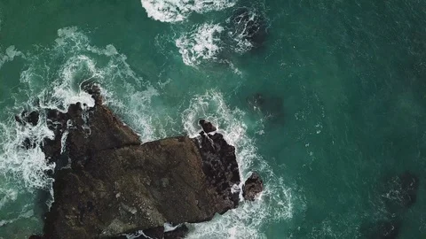 Waves splash against rock formations viewed from above as camera rotates Video stock 104253362