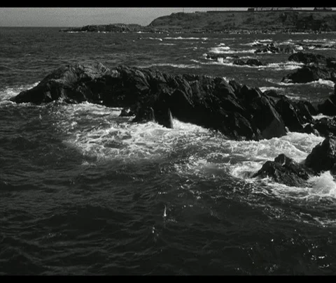 Waves splash over rocky coastline, light house in distance, Scotland, UK 1950 Stock Footage 131077645