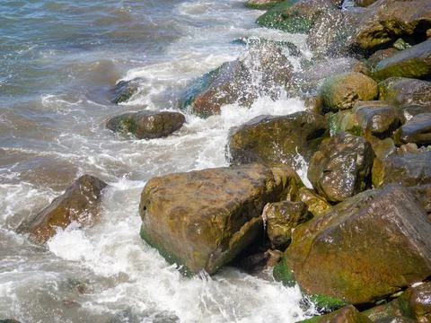 Waves with splashes fall on large stones. Shore view. Beautiful stones that s Stock Photos