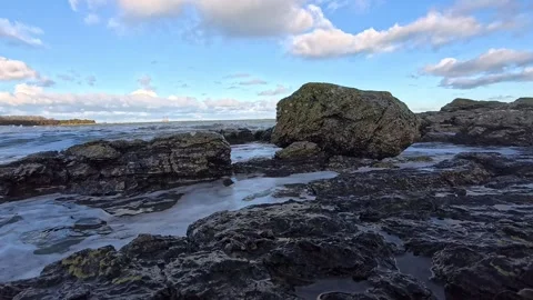 Waves splashing in slow motion surround shaded beach rock boulders Stock Footage 325720716