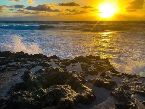 Waves spray up through rocks on the beach at sunrise Stock Photos