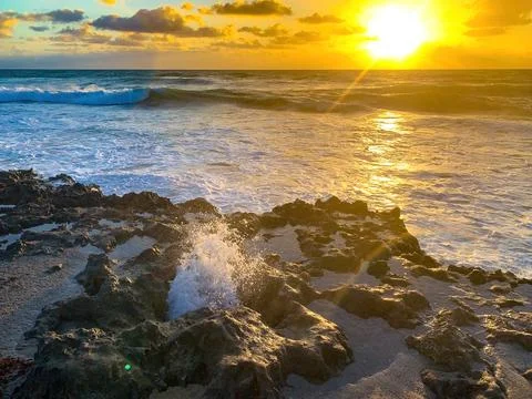 Waves spray up through rocks on the beach at sunrise Stock Photos