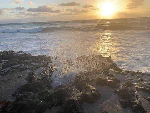 Waves spray up through rocks on the beach at sunrise Stock-Fotos