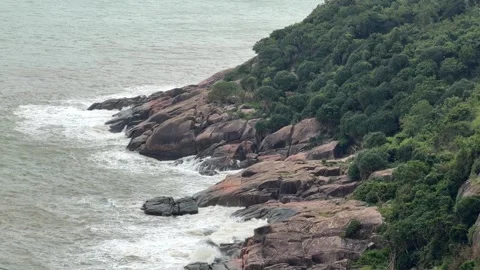 Waves strike rugged coastal rocks as powerful surf spreads white foam across the Video stock 324957064
