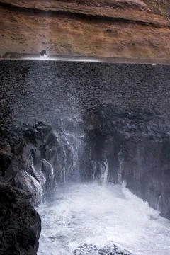 Waves strike volcanic cliffs by stone sea wall on Madeira coast Stock Photos