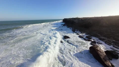 Waves surge against rugged cliffs under clear blue sky Video stock 346076394