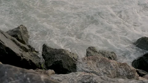 Waves swirl and strike hard against jagged rocks during slow motion coastal Stock Footage 307696136