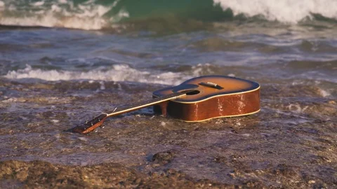 Waves throw guitar on empty shore or stone beach. Tide brings the guitar ashore Stock Footage 126948212