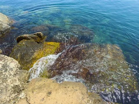 Waves touching rocks along a clear blue sea near the shore on a sunny day Foto stock